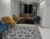 مبلمان سرمه ای و زرد و صندلی چوبی و سقف نورپردازی شده بانور سفید سالن نشیمن آپارتمان در بندرعباس